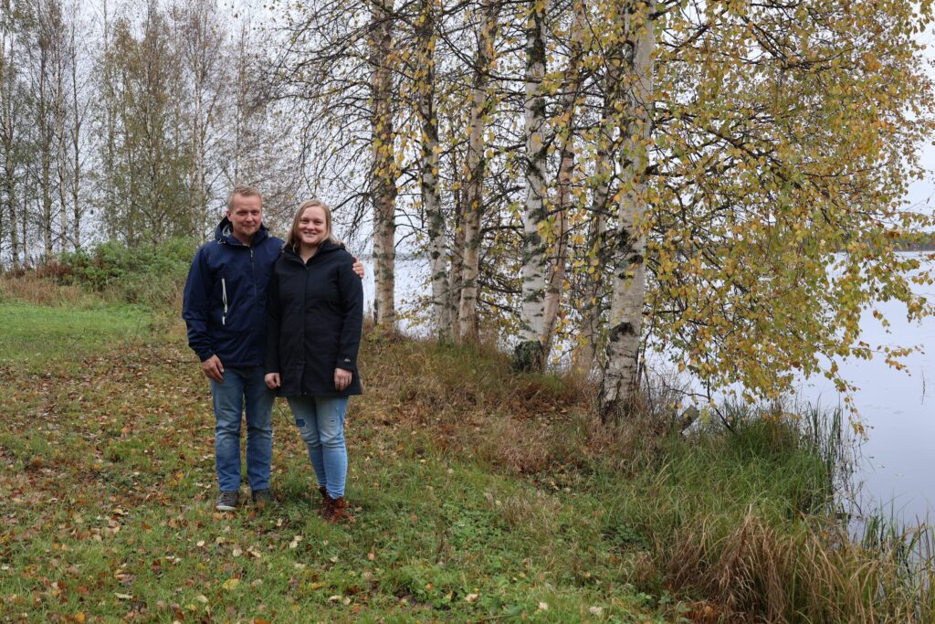 Kuvassa Hiltusen pariskunta Kortteisen rannalla. Taustalla näkyy koivuja, joissa on keltaisia ja vihreitä lehtiä.